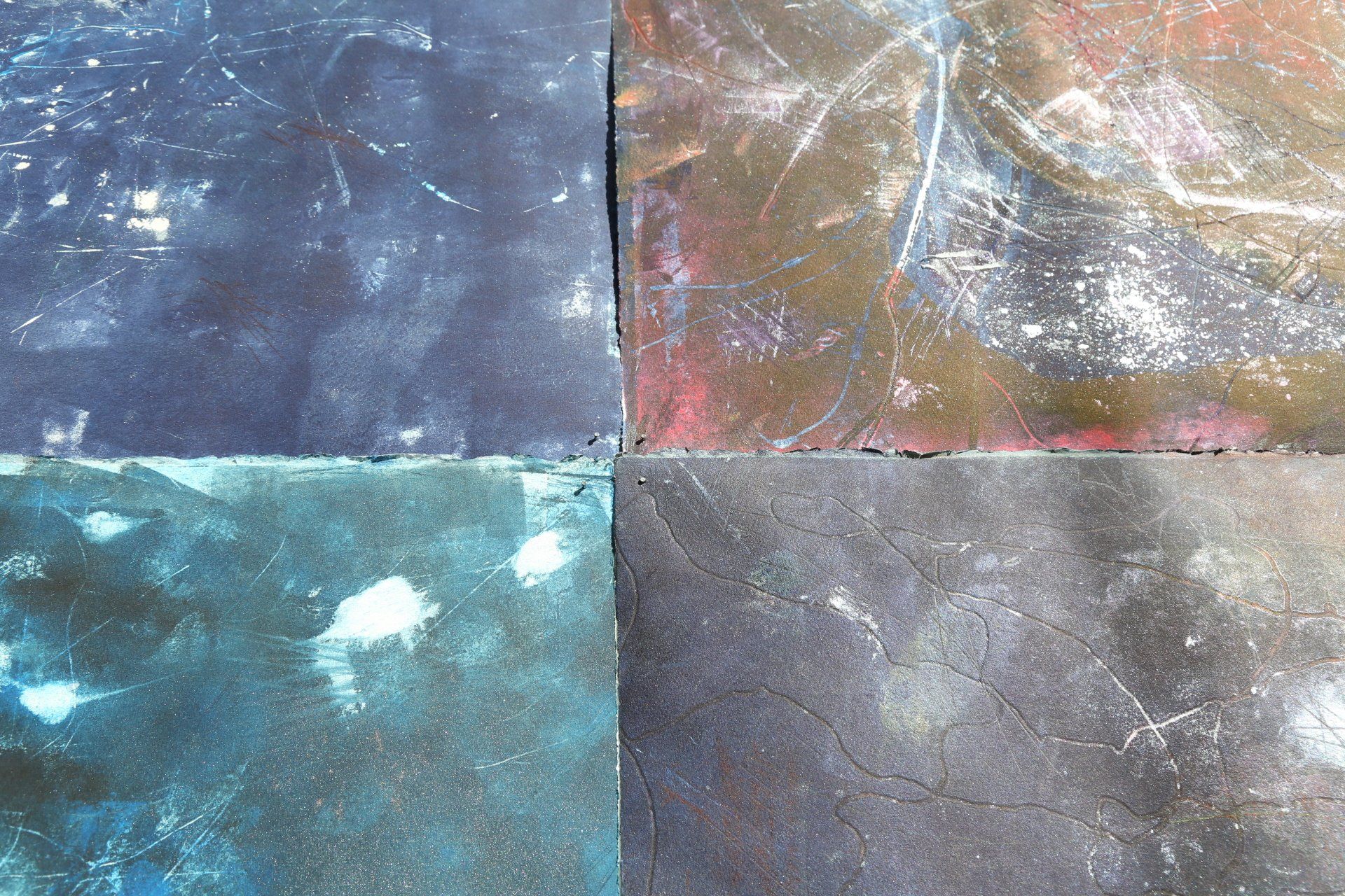 Four worn, square panels in blue, brown, and grey hues, scratched and stained with white markings.