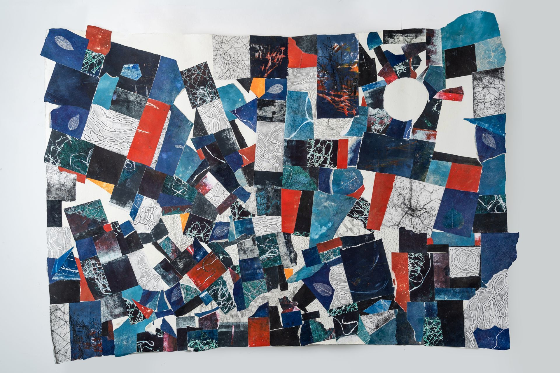 Abstract collage of overlapping blue, red, and black paper shapes with a white circle on a white background.