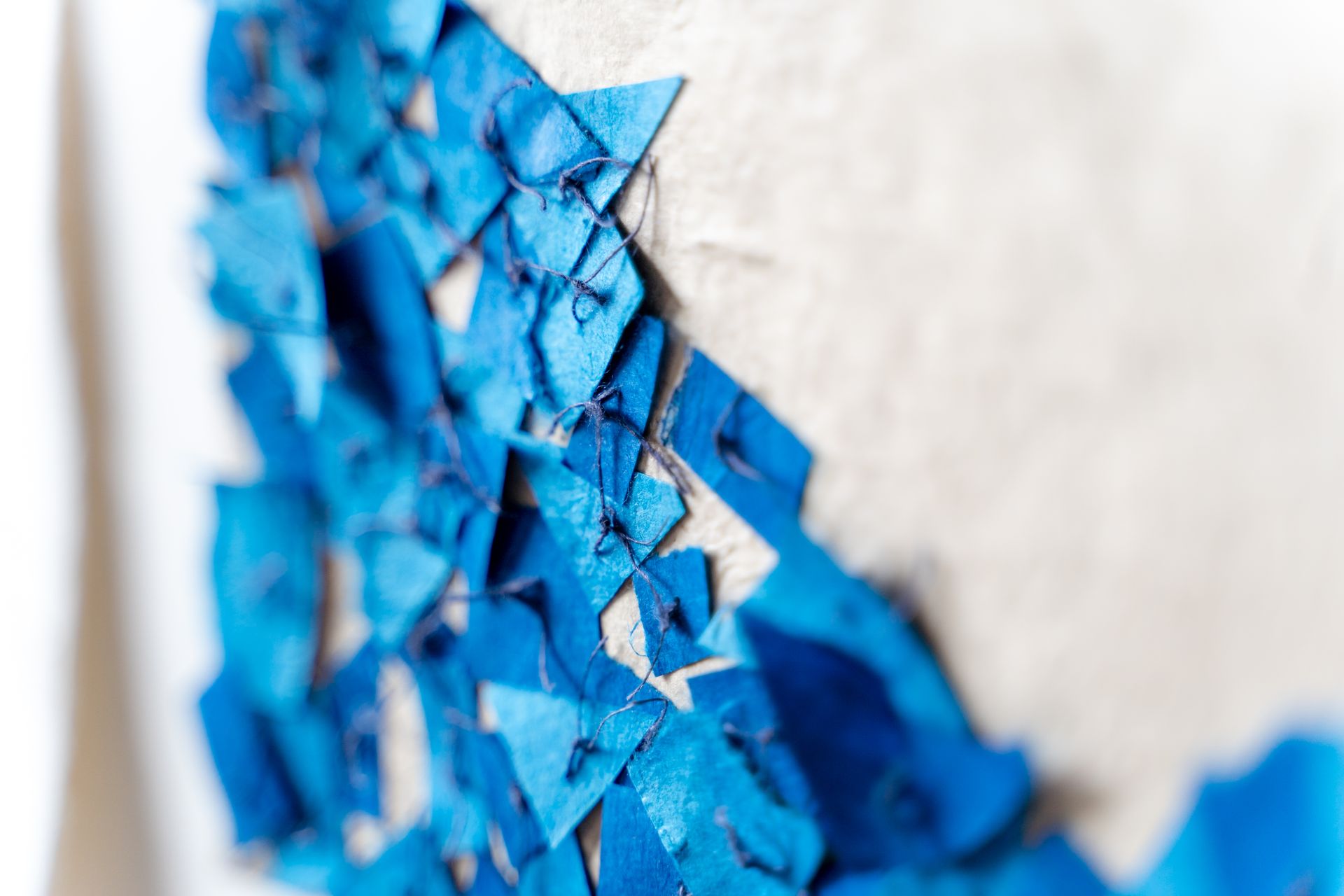 Blue paper shards sewn onto a white surface, creating an abstract composition.