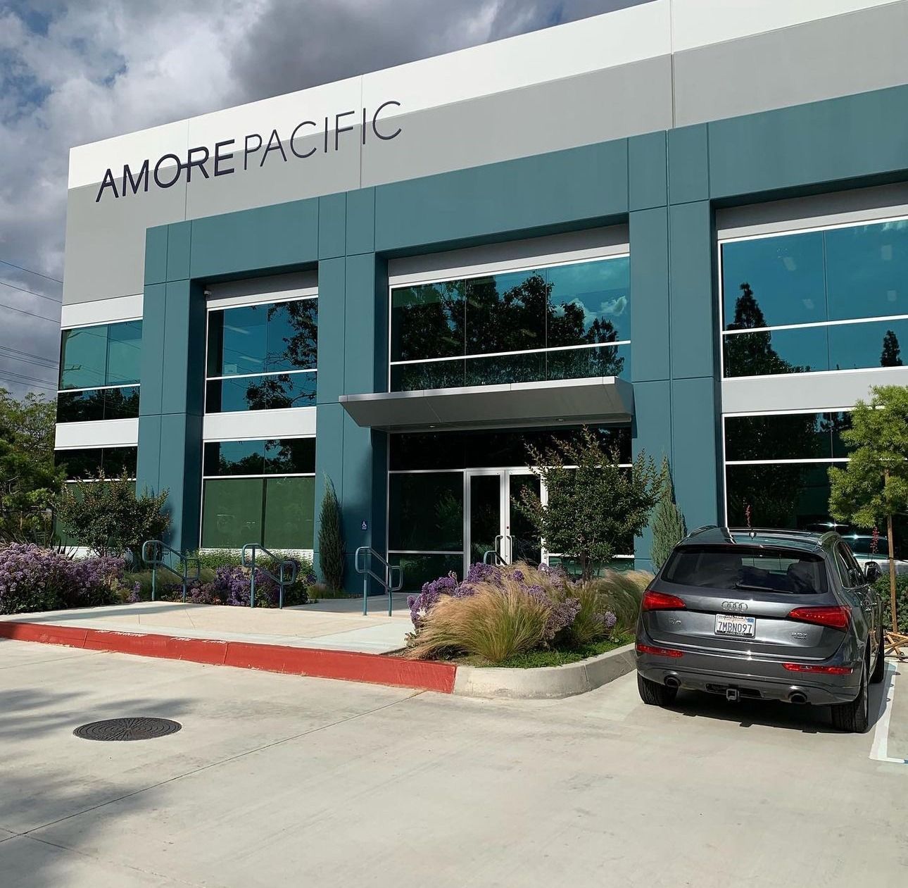 Modern office building with AMOREPACIFIC sign, large glass windows, landscaping, and a parked car in front