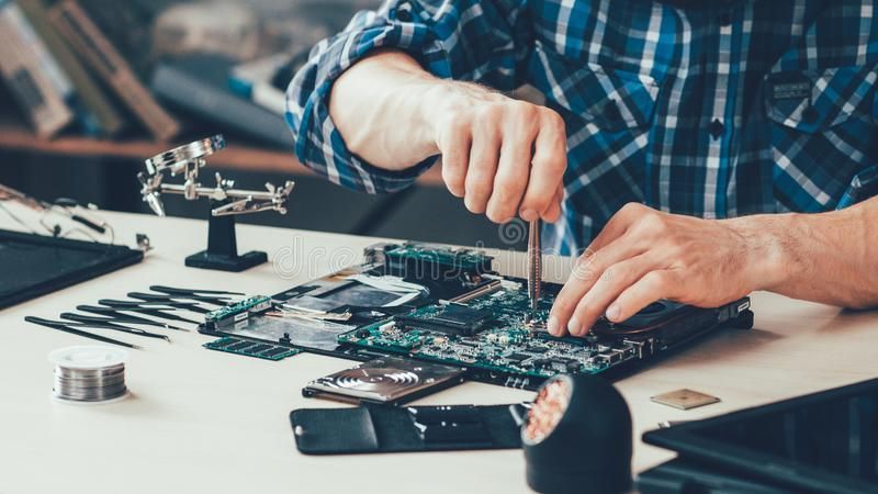 A person working on a circuit board with a screwdriver. A desk with tools and computer parts.