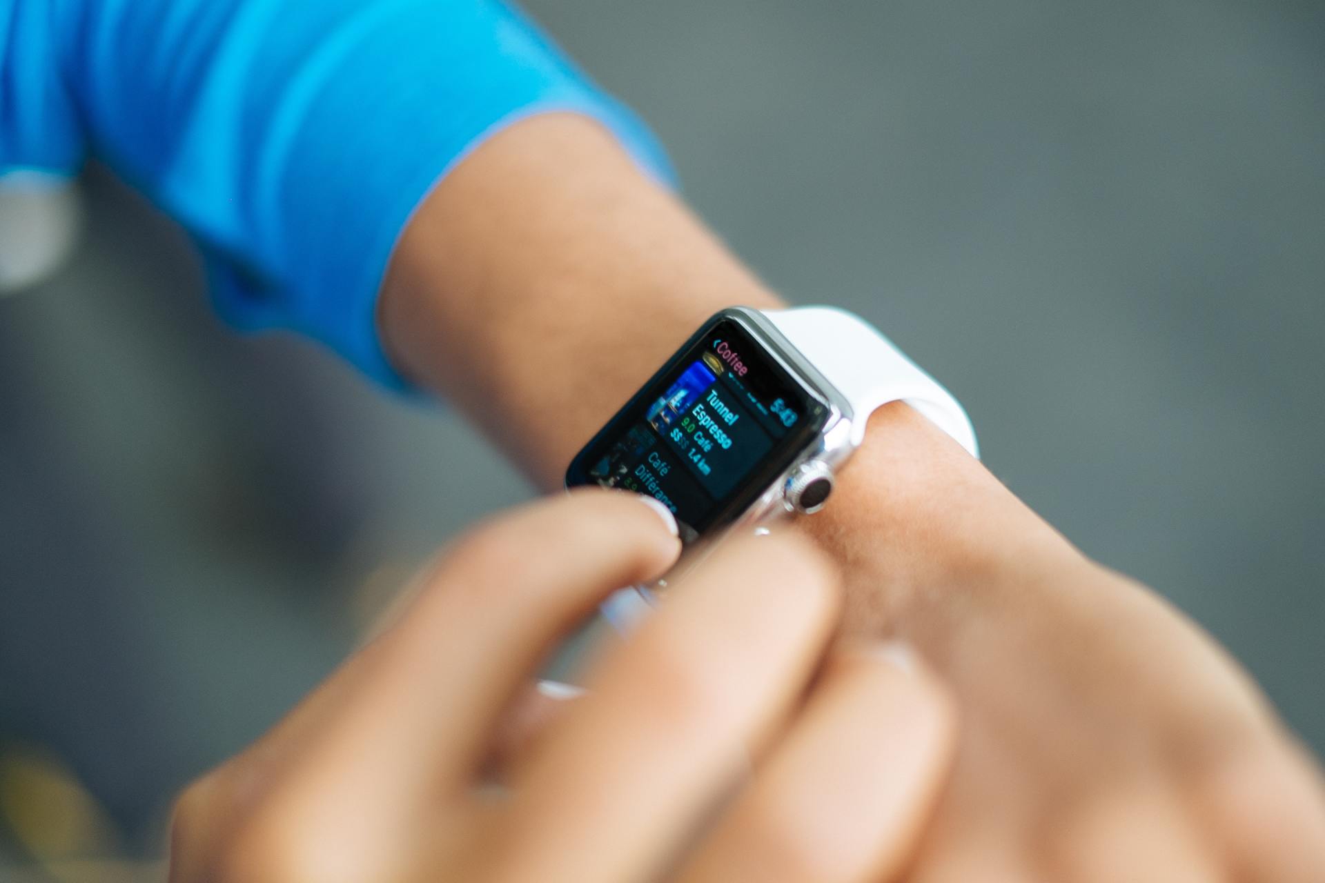 Person using a smartwatch with a white band, touching the screen. Blue sleeve visible.
