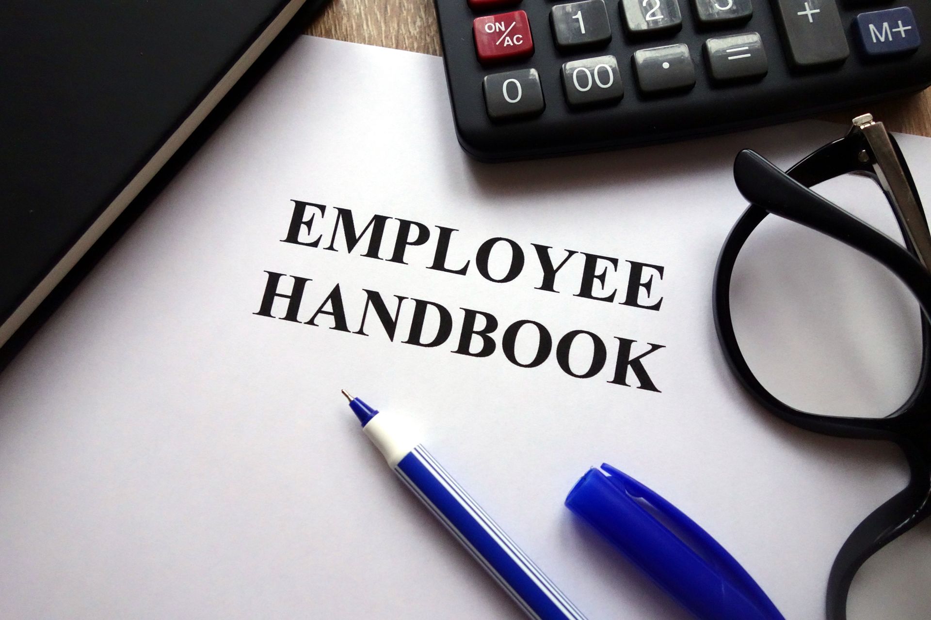 An employee handbook with a pen glasses and a calculator