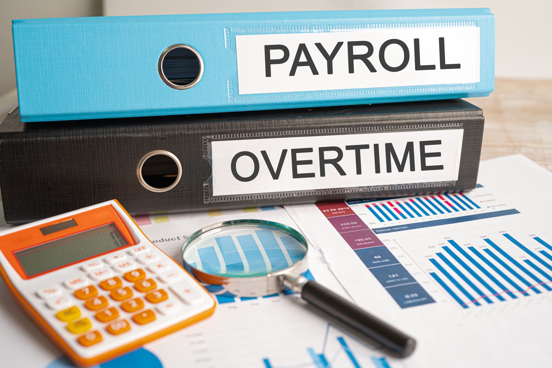 A calculator , magnifying glass , pen and binders with the words payroll and overtime on them.