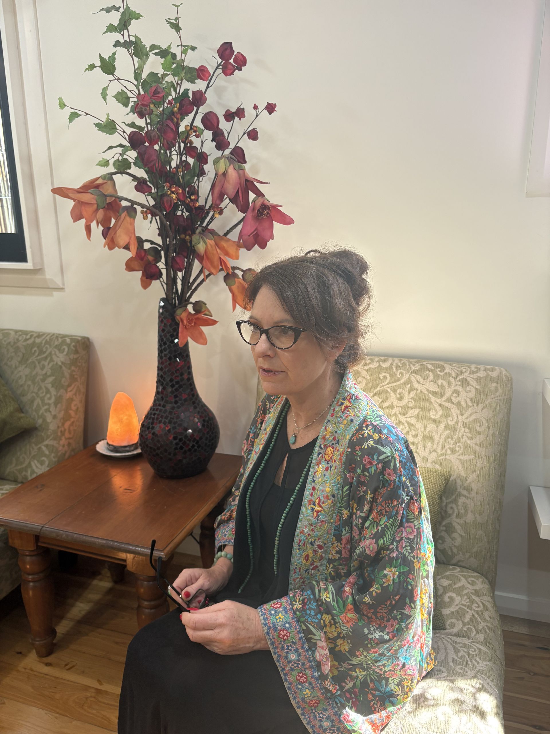 Woman seated in a room, wearing glasses and a colorful shawl, holding glasses — Mind Guidance Centre in Wangi Wangi, NSW