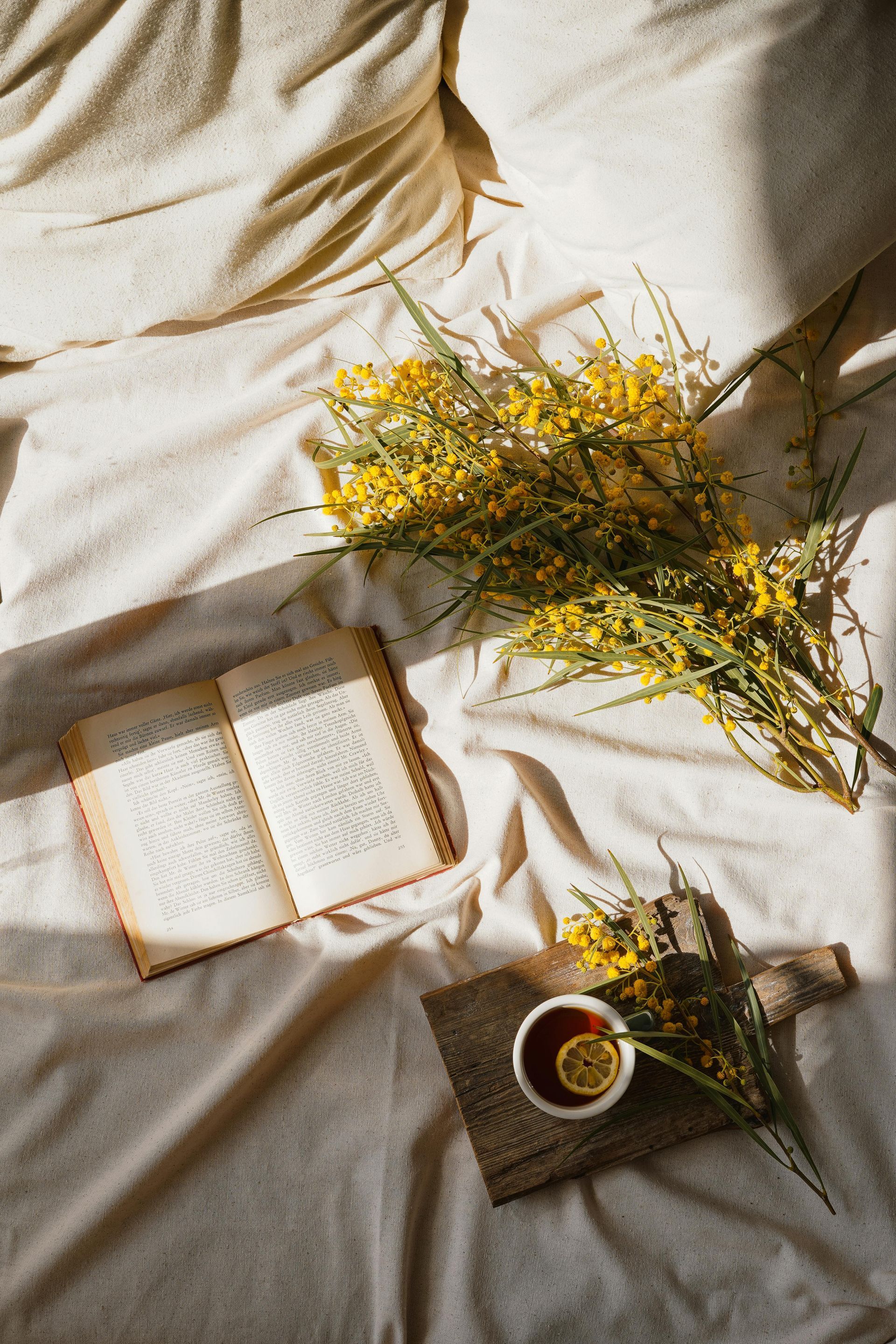 Open book, tea with lemon, and yellow flowers on a bed with beige sheets — Mind Guidance Centre in Wangi Wangi, NSW