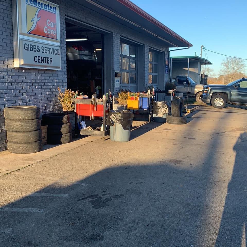 Exterior of Gibbs Service Center with tires, tools, and a truck. Bright sunny day.