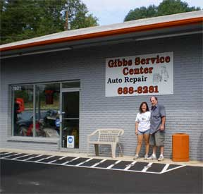 Exterior of Gibbs Service Center with two people posing in front. Grey building with a sign and orange accents.