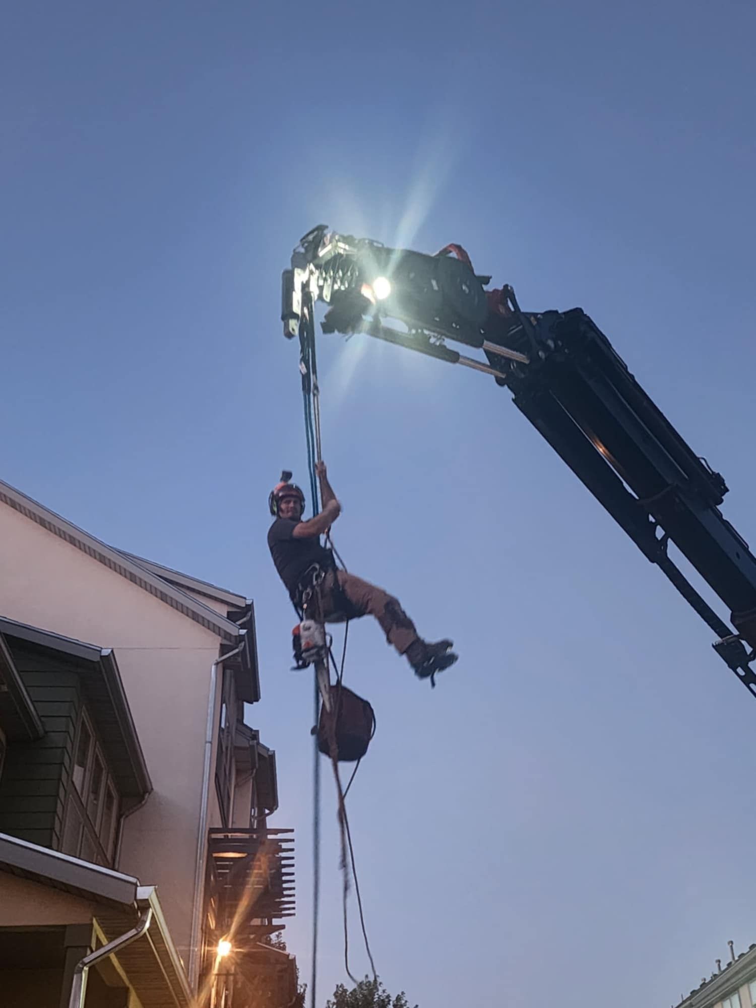 Man suspended from crane, working on building facade at dusk.