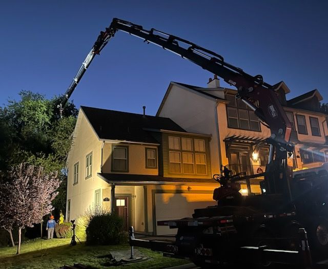 Crane trimming tree near a two-story house at dusk.