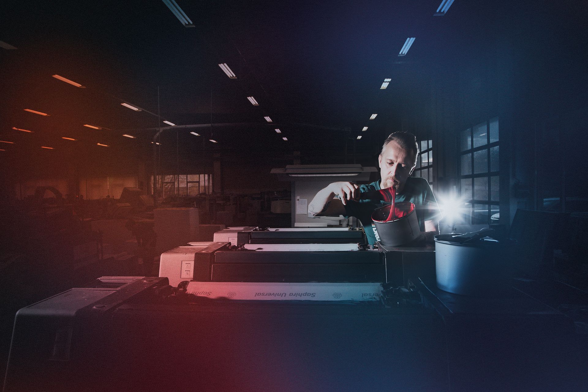 Person arbeitet in einem schwach beleuchteten Industrieraum; rotes und blaues Licht.