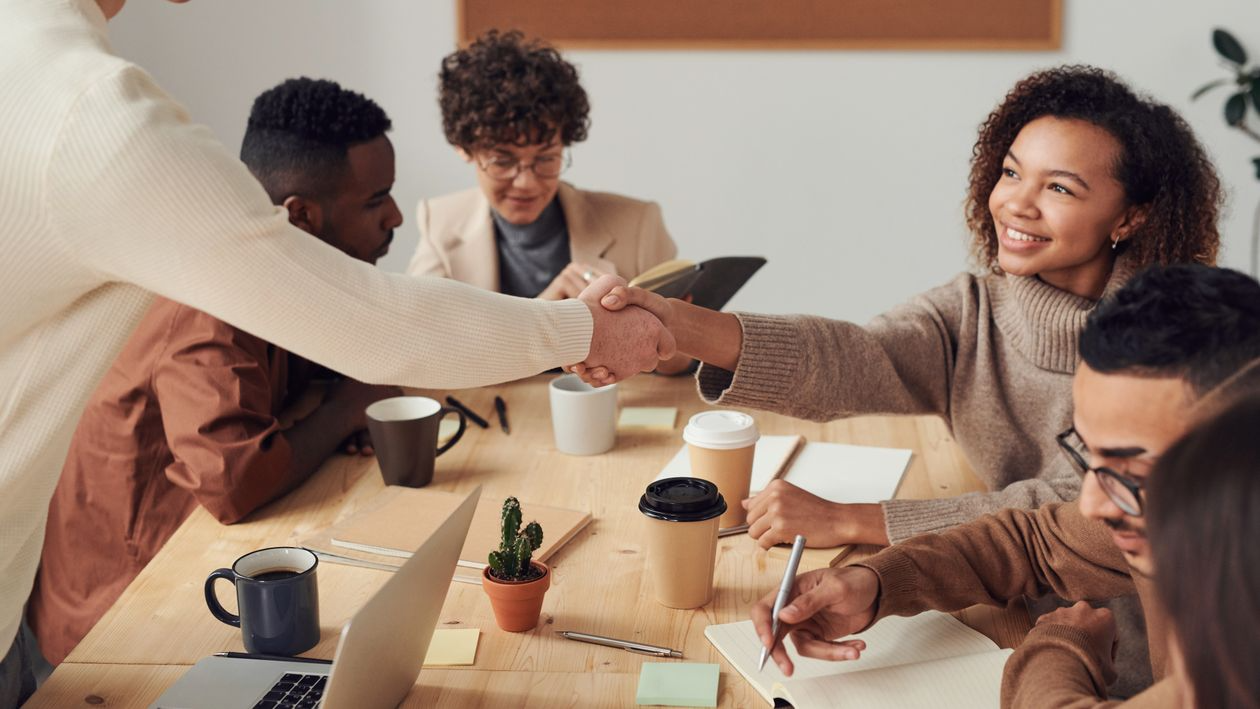 Team members shaking hands during a collaborative meeting, representing trust, alignment, and workfo