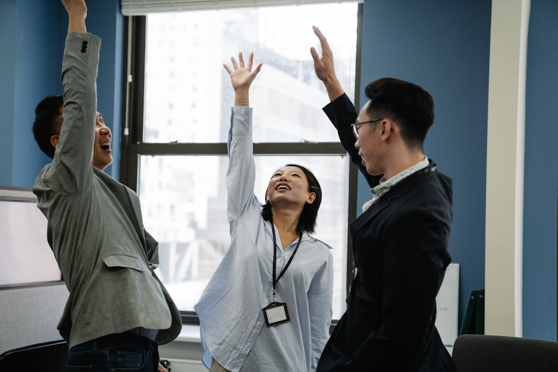 Three colleagues celebrating success in an office, raising their hands after achieving a shared goal.
