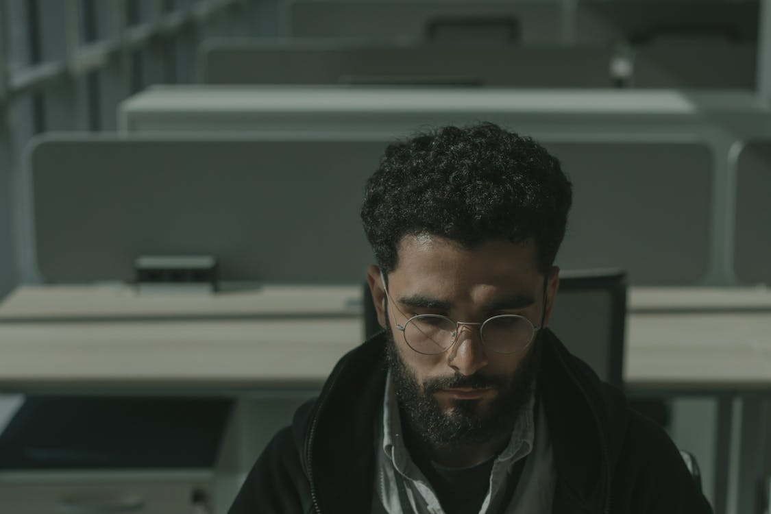 Man with glasses sitting at an office desk, looking fatigued while working, illustrating the need for employee engagement solutions.
