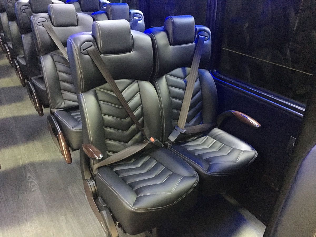 A row of black leather seats with seat belts on a bus.