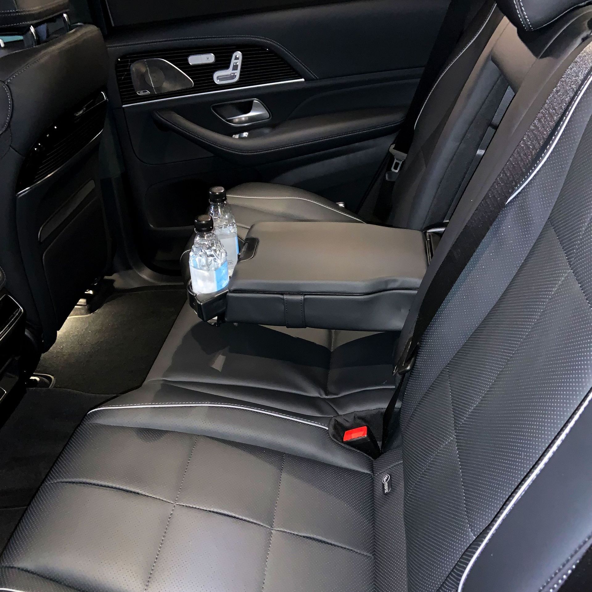 The back seat of a car with a bottle of water on the arm rest