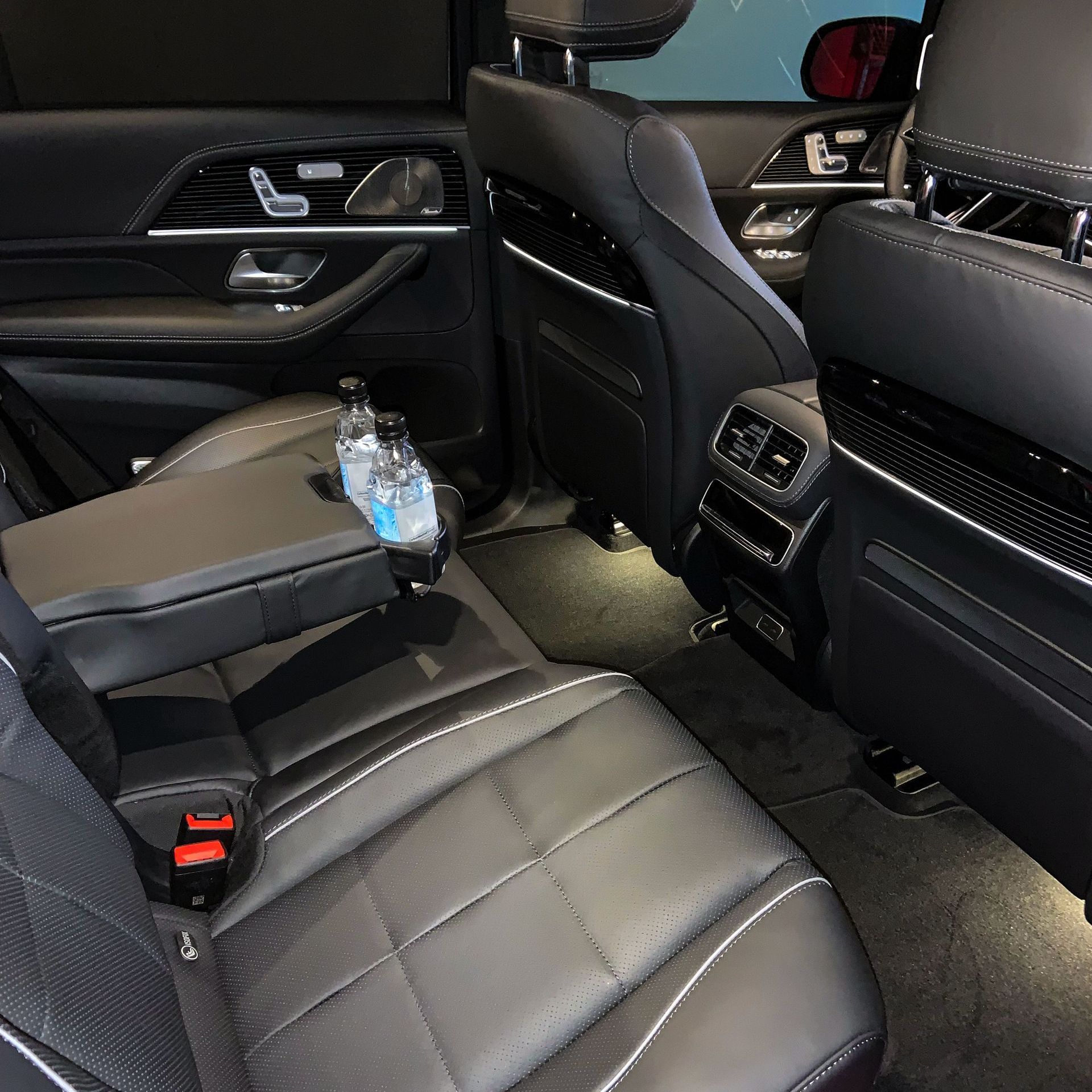 The back seat of a car with a bottle of water in the arm rest
