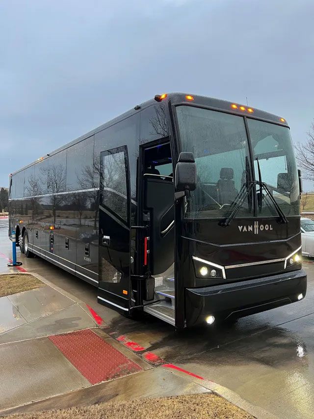 A large black bus is parked in a parking lot on a rainy day.