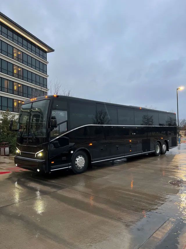 A black bus is parked in a parking lot in front of a building.