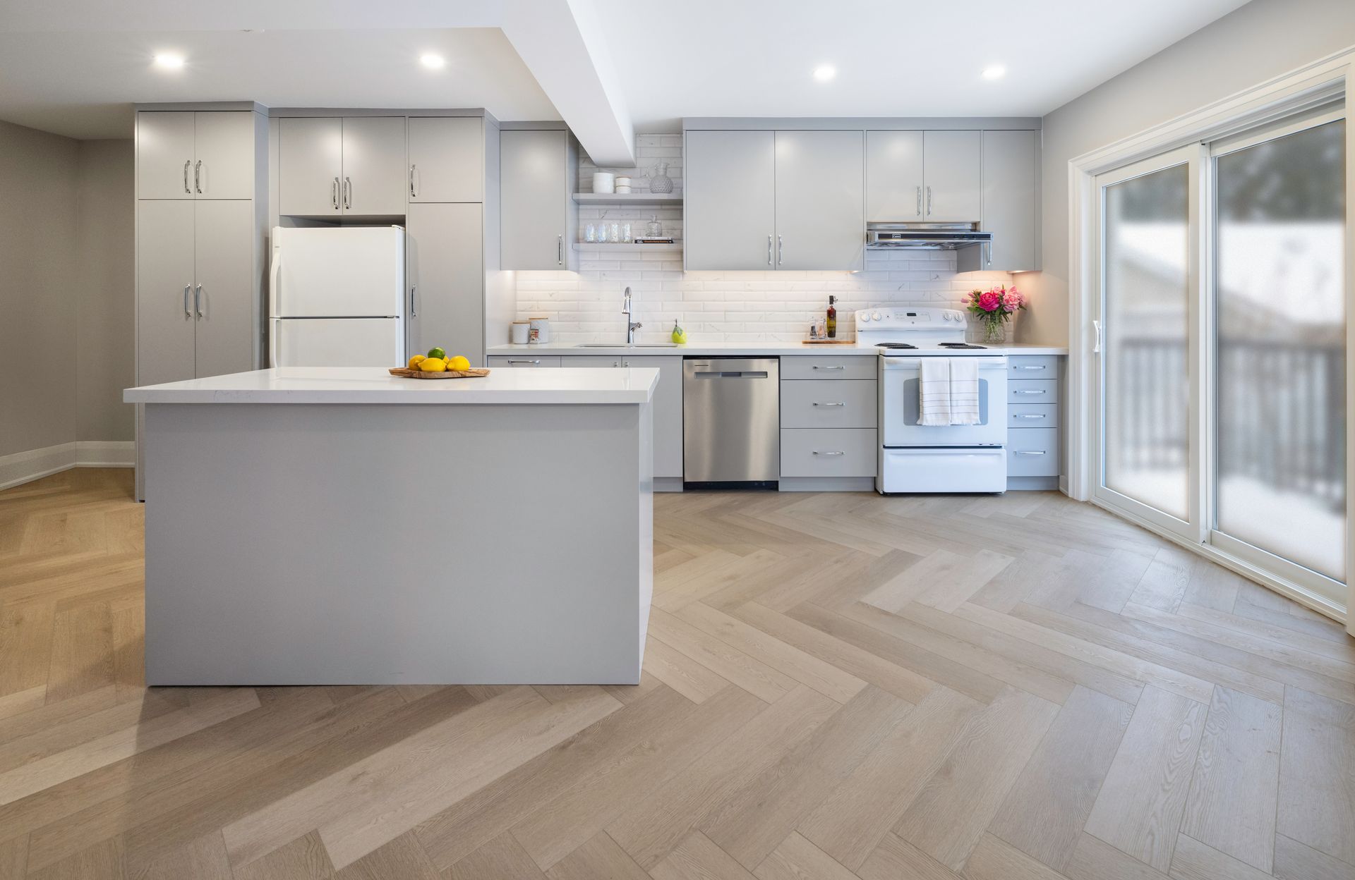 Modern gray kitchen with an island, cabinets, appliances, and herringbone flooring.