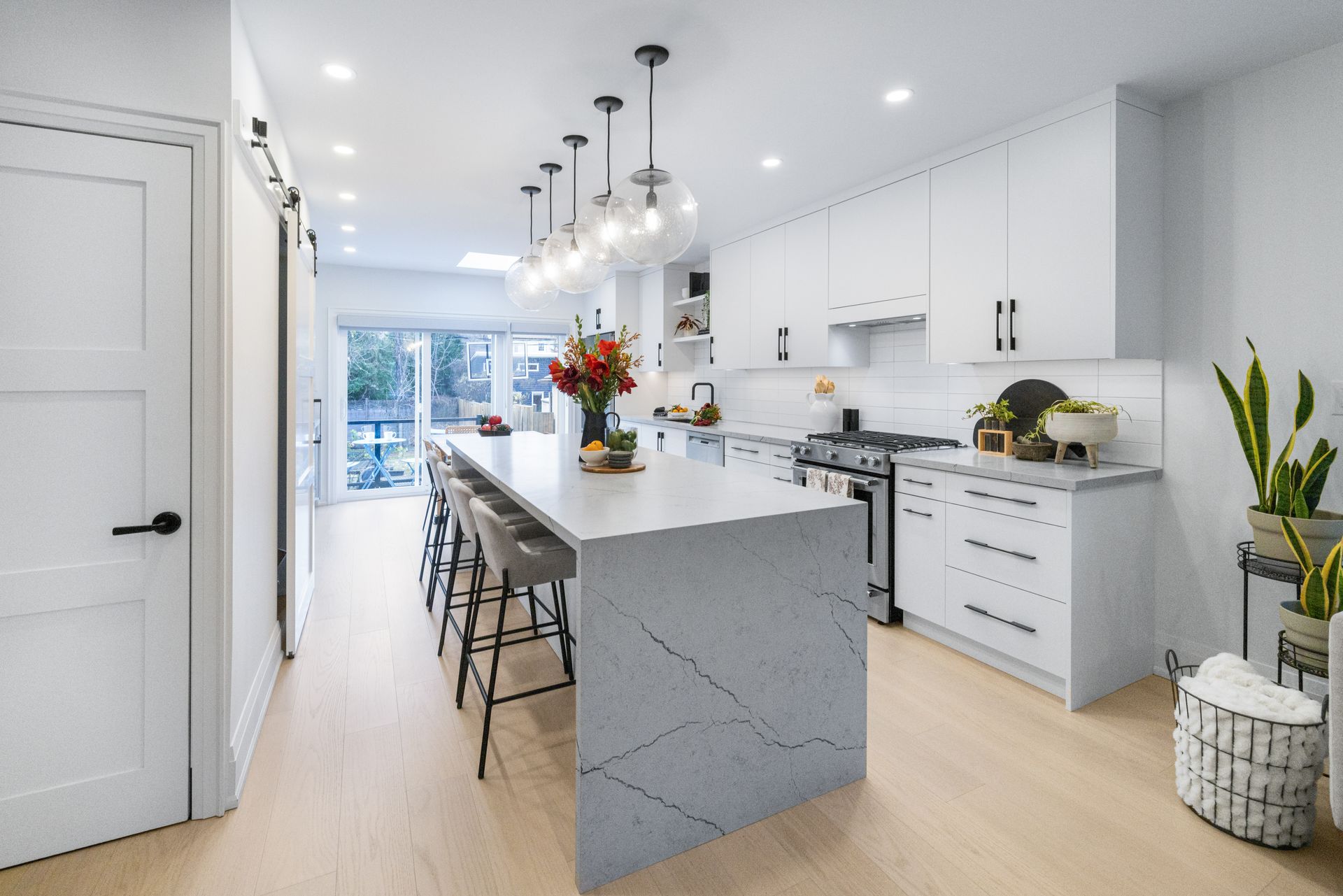 Modern white kitchen with island, seating, and overhead lights; light wood floors.