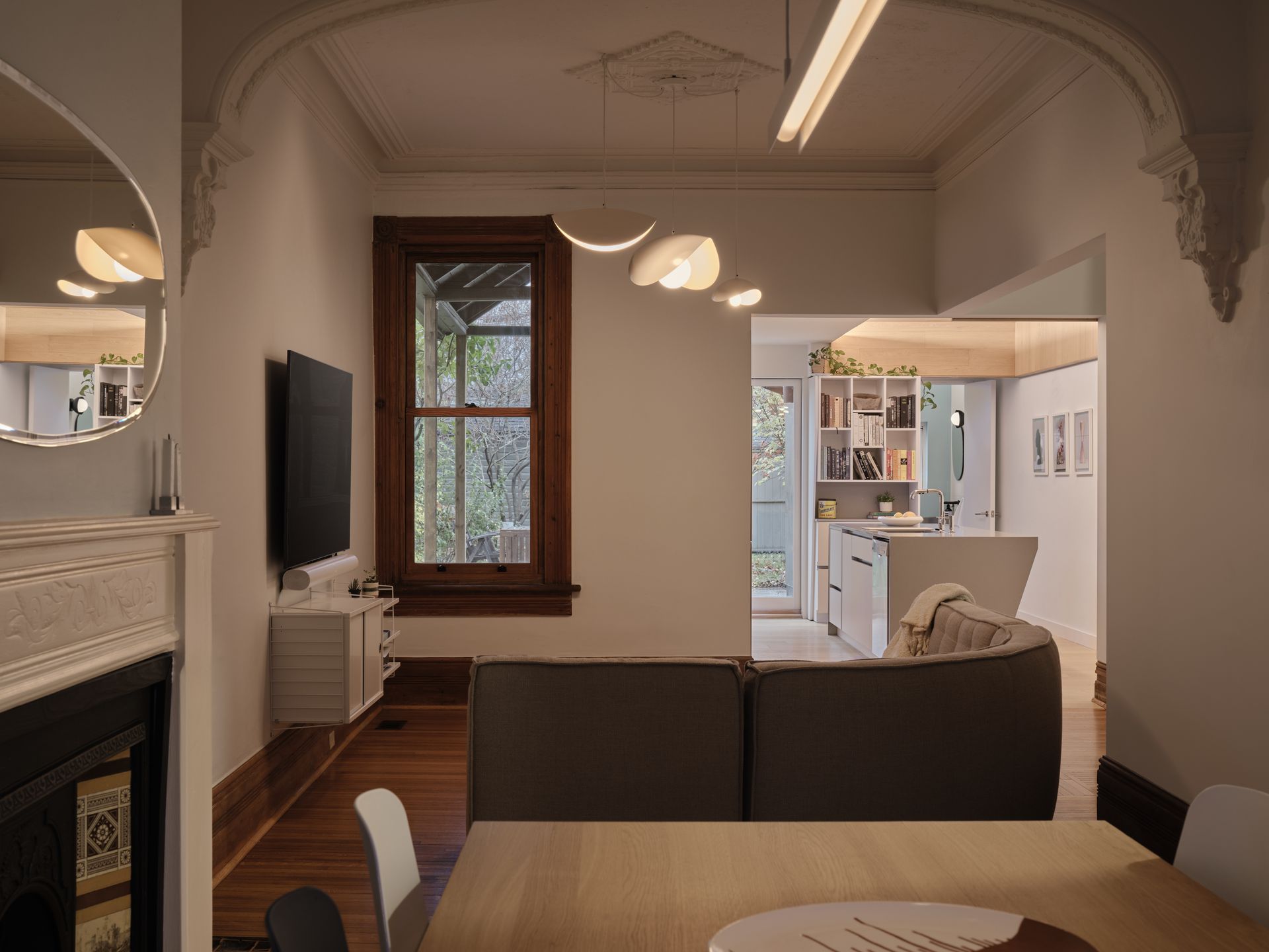 Living room with a dark-brown sofa, wooden floor, and a view into a bright kitchen.