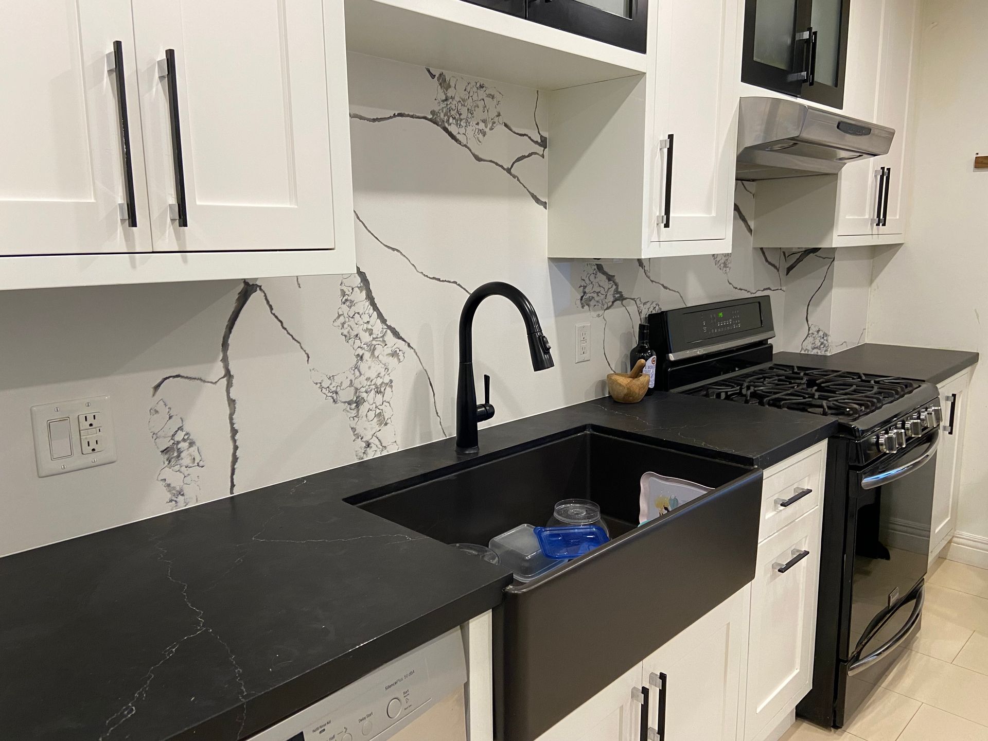 Modern kitchen with black countertops, sink, and appliances; white cabinets, and marble-look backsplash.