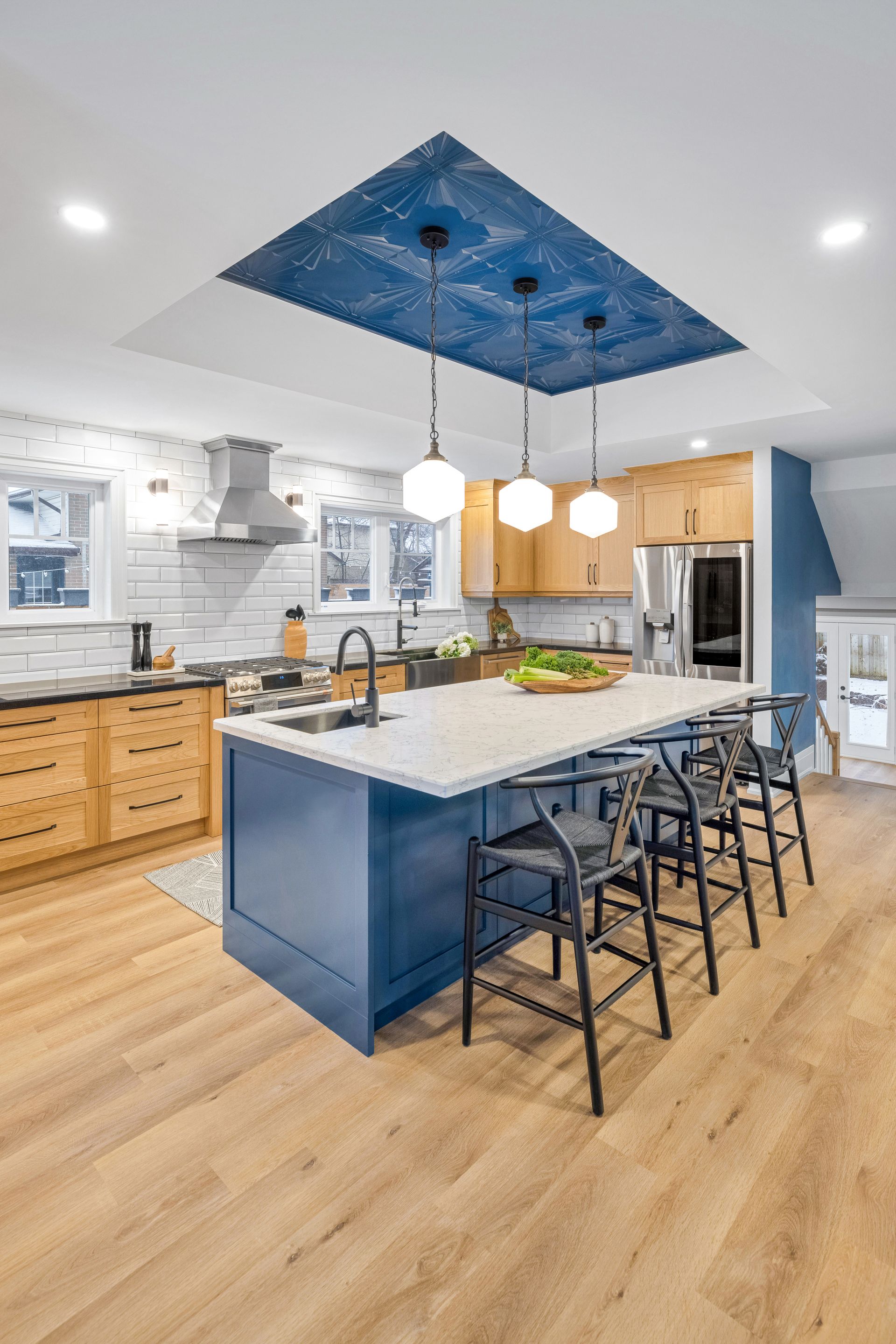 Modern kitchen with blue island, light wood cabinets, and patterned blue ceiling.