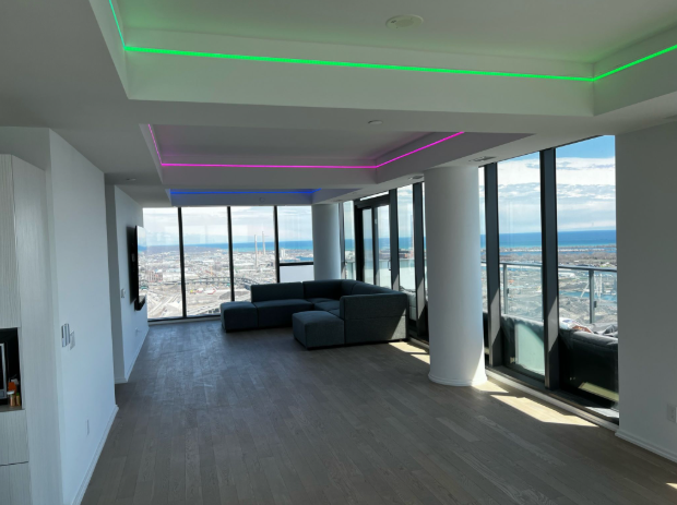 Modern empty living room with floor-to-ceiling windows, city and ocean views, and colorful ceiling lights