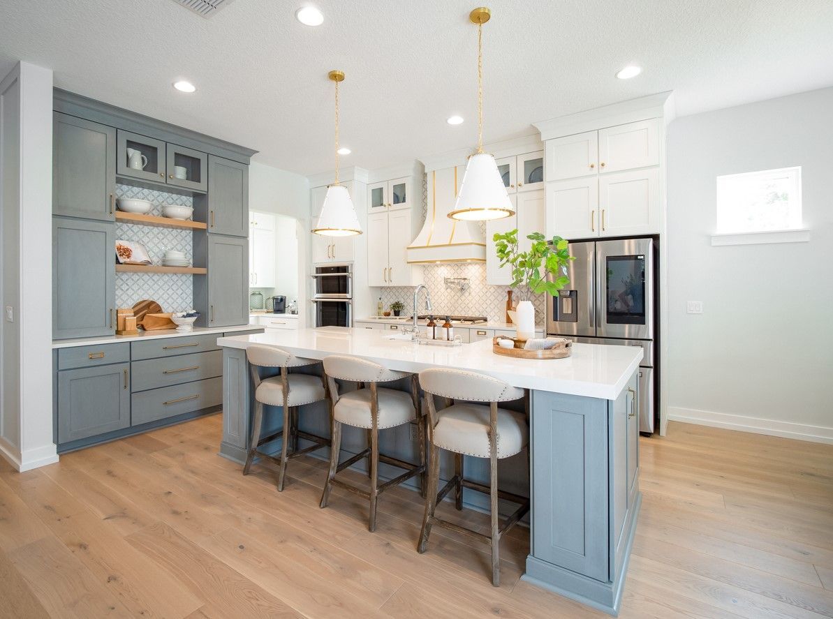 Stylish kitchen with blue and white cabinets, large island with stools, and gold pendant lights.
