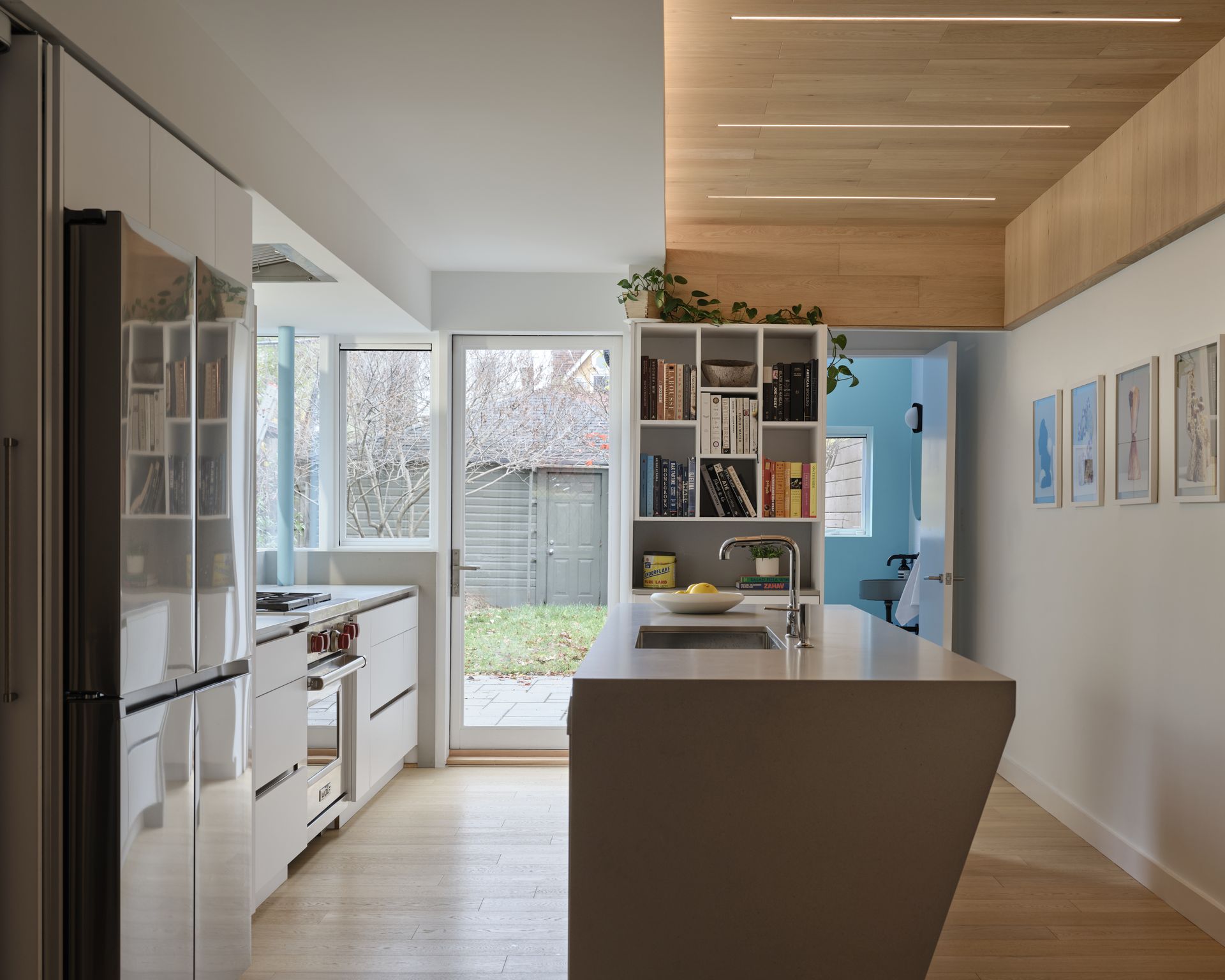 Modern kitchen with light wood floor, white cabinets, and island; door to backyard.