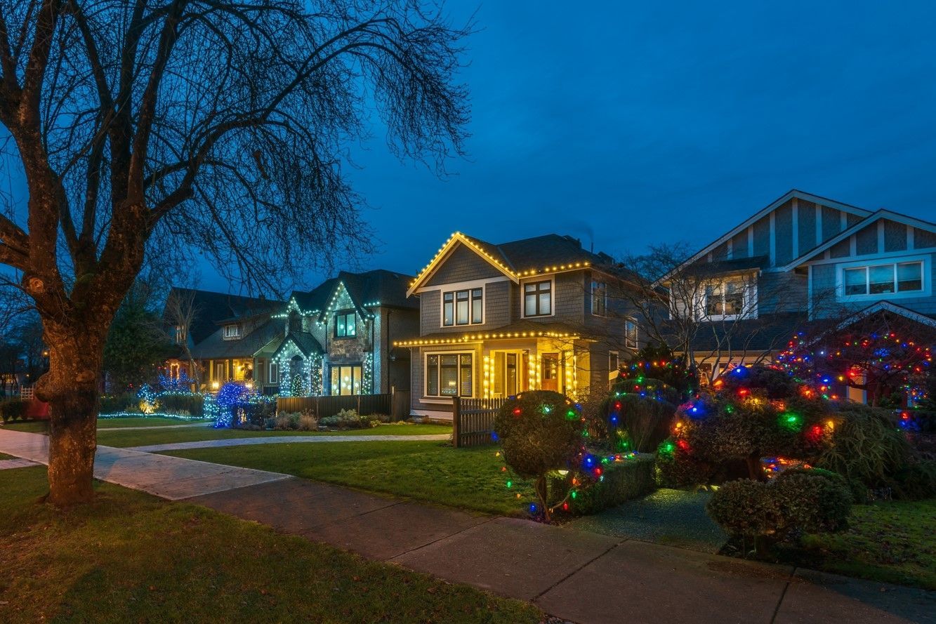 Houses on a street at dusk, decorated with colorful Christmas lights.