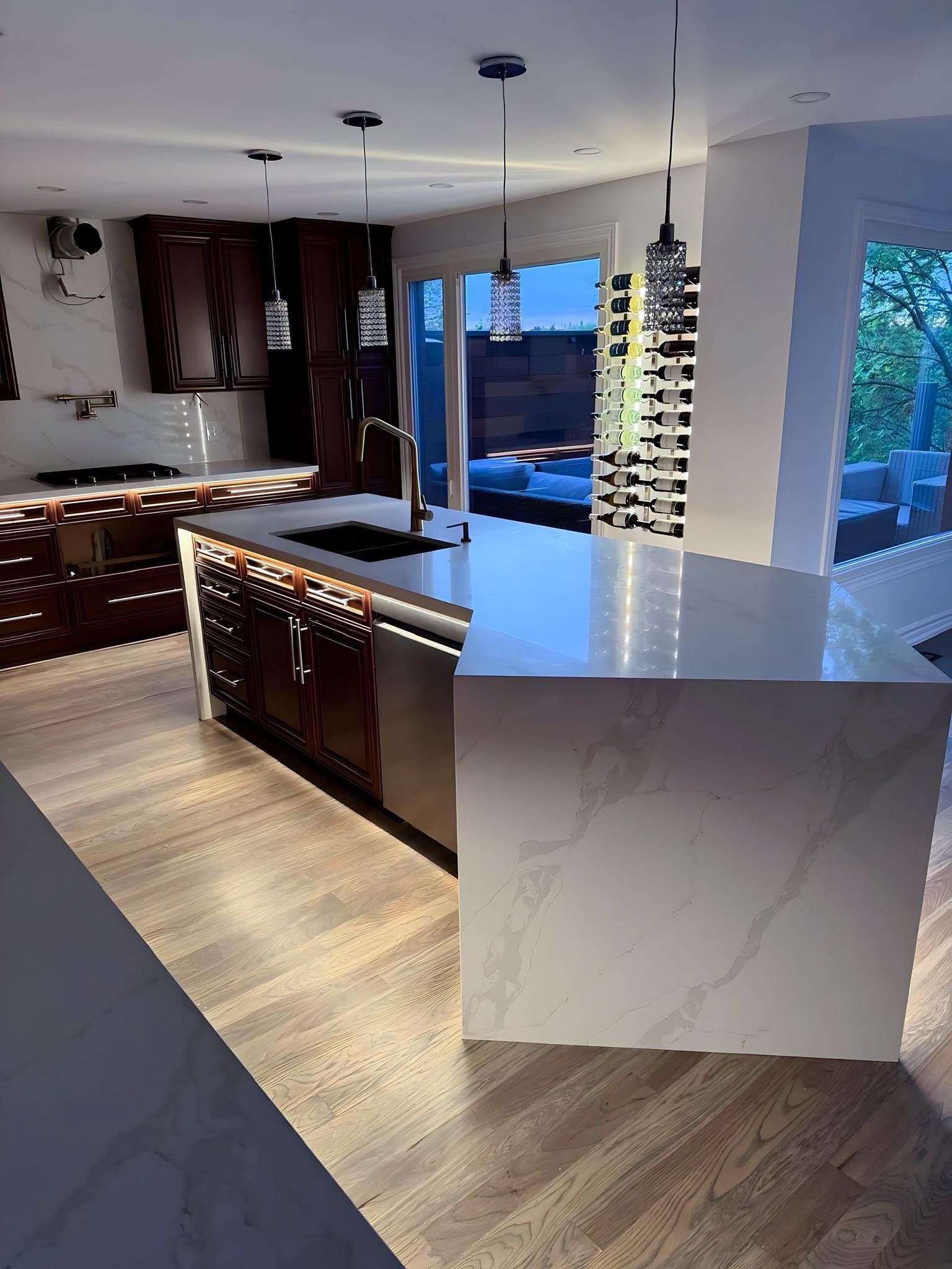 Modern kitchen with dark cabinetry, white island, wood floors, and outdoor access.