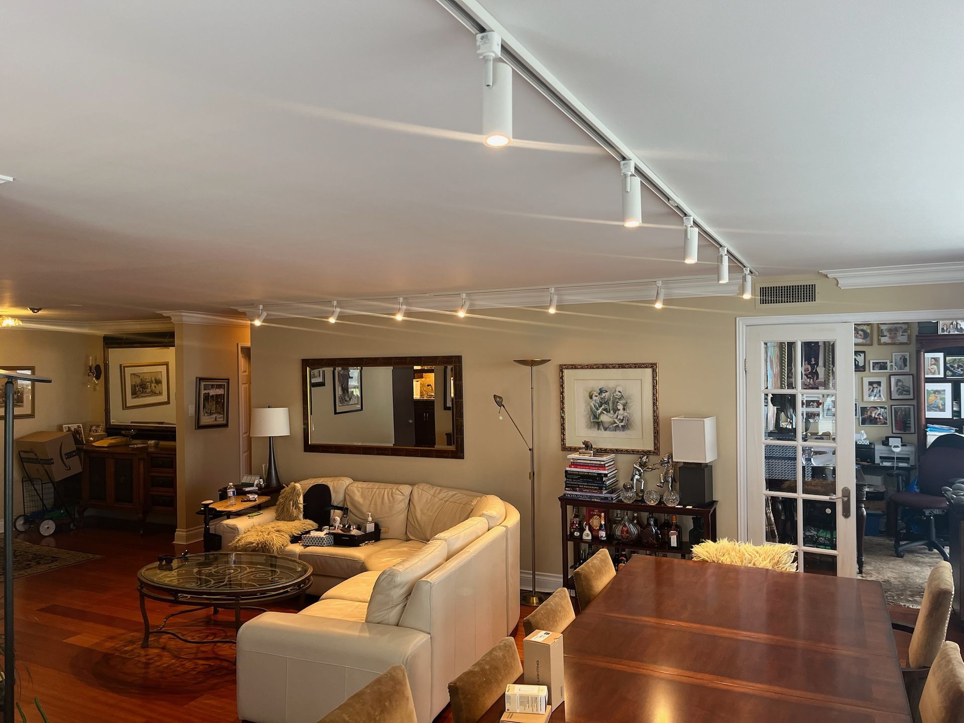 Living room with cream sectional, track lighting, wood floor, and dining table.