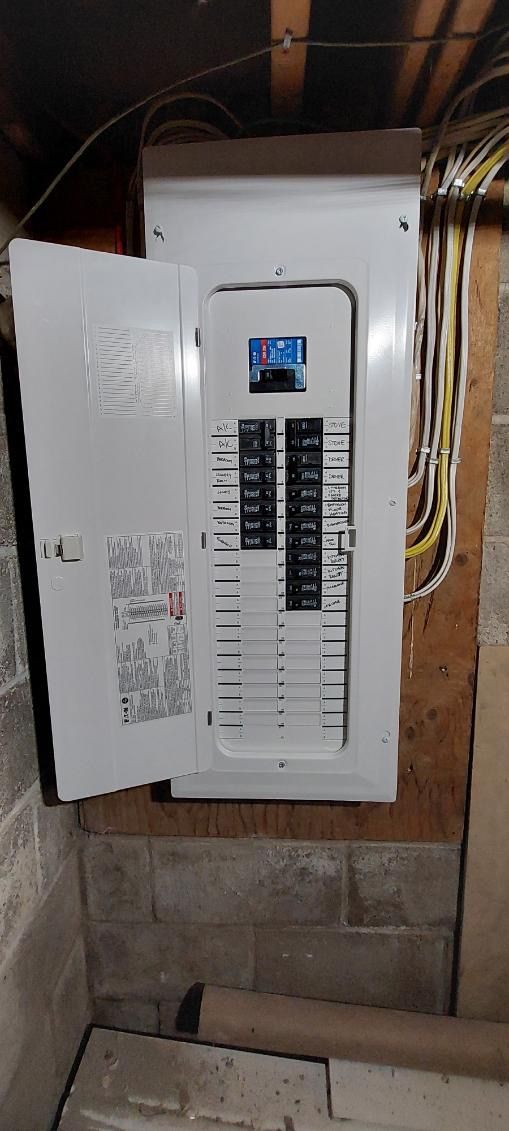 An open electrical panel in a basement. The door is open revealing circuit breakers. Brown wall and cement block.