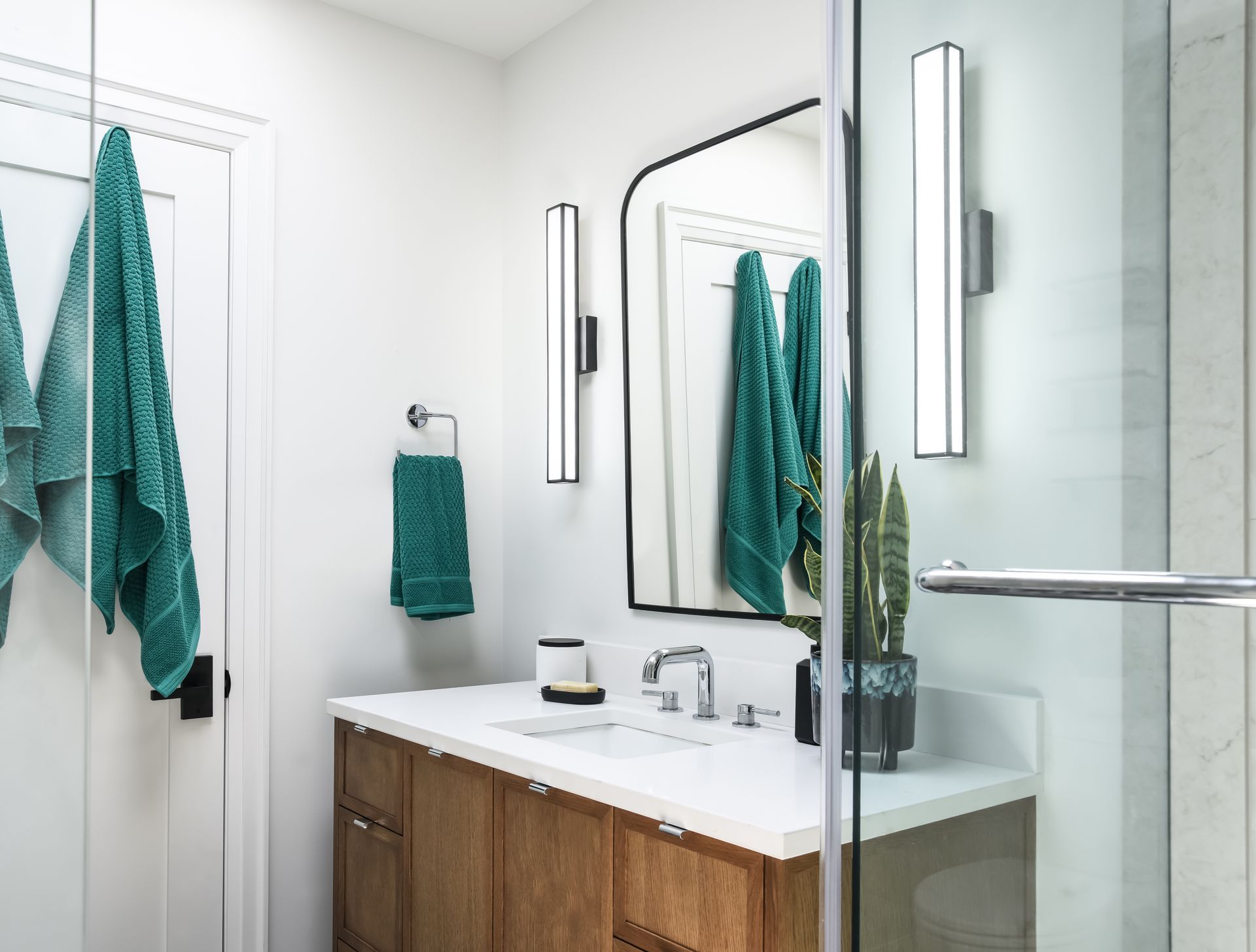 Bathroom with wooden vanity, teal towels, arched mirror, and modern lighting.