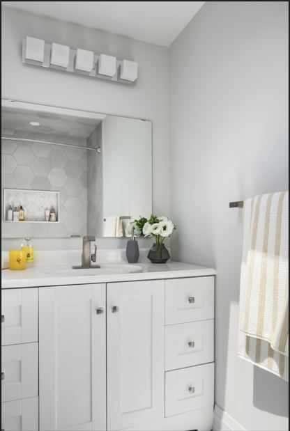 White bathroom with vanity, mirror, and a towel on a bar. Gray wall and light fixture.
