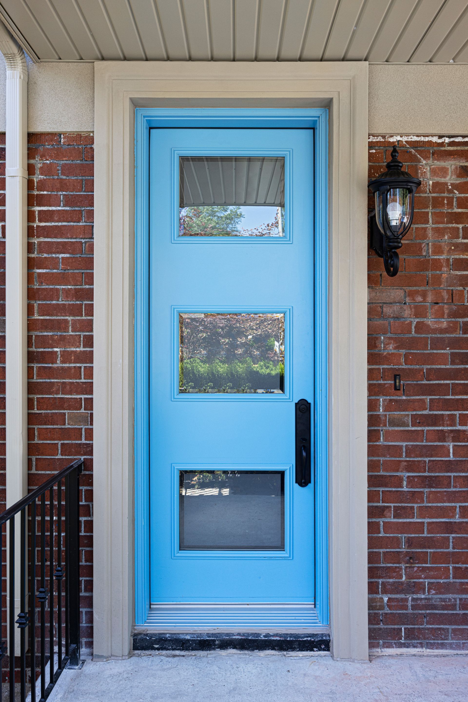 Blue front door with three glass panels, set in brick with a black handle and a wall-mounted light.