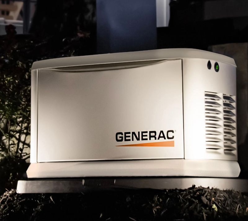 White Generac home generator with orange logo, outdoors at night.