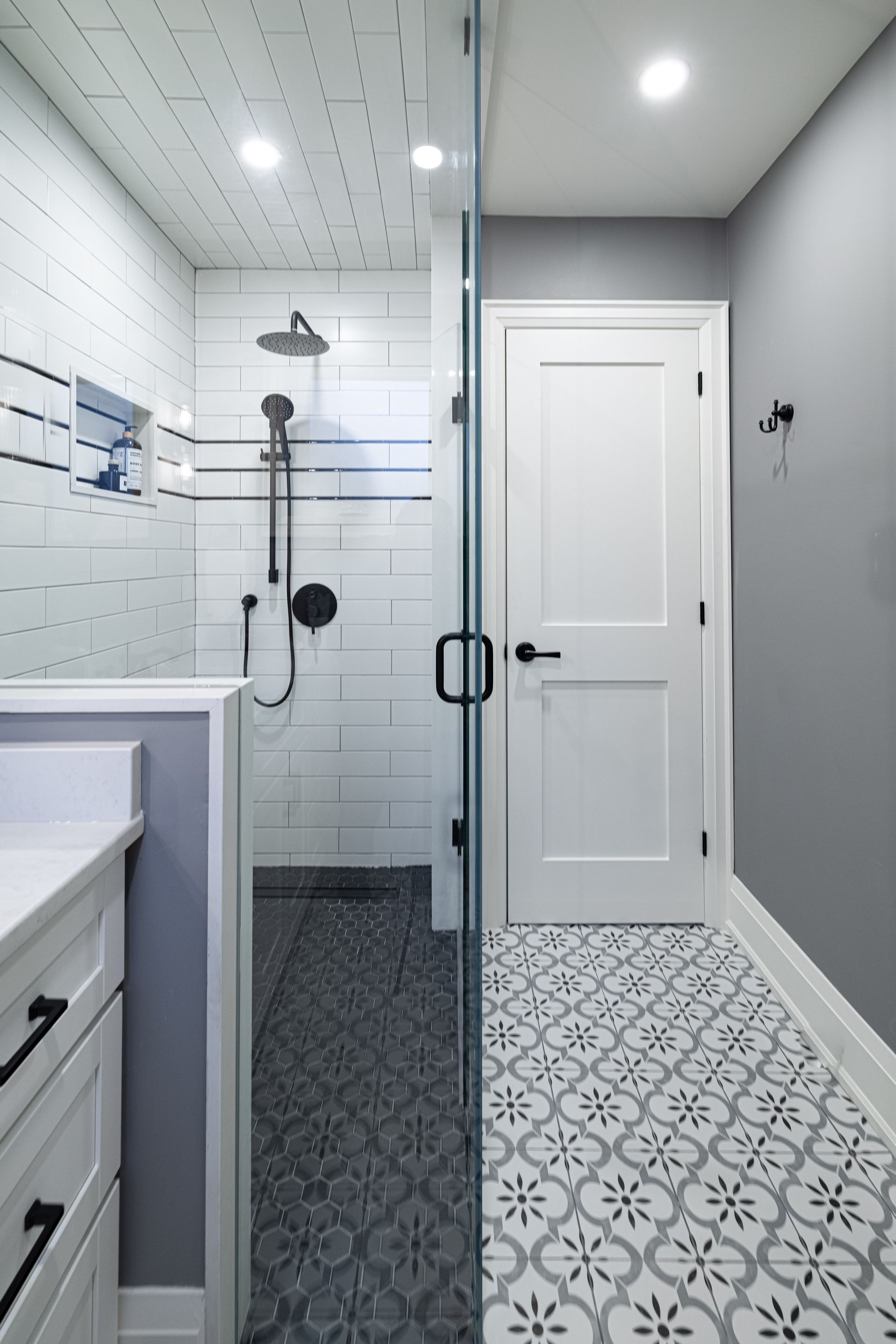 Bathroom with white shiplap shower, patterned floor tiles, glass shower door, white vanity, and gray walls.