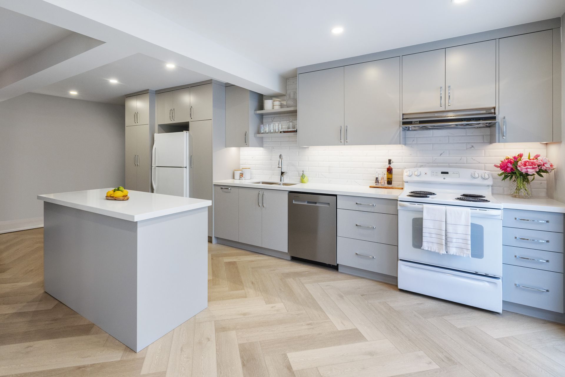 Modern gray kitchen with an island, white appliances, and wooden floors.