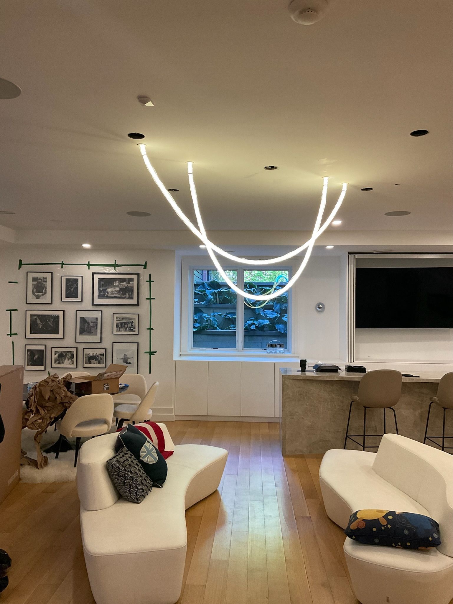 Modern living room with curved white sofas, wood floor, and illuminated arching ceiling lights.