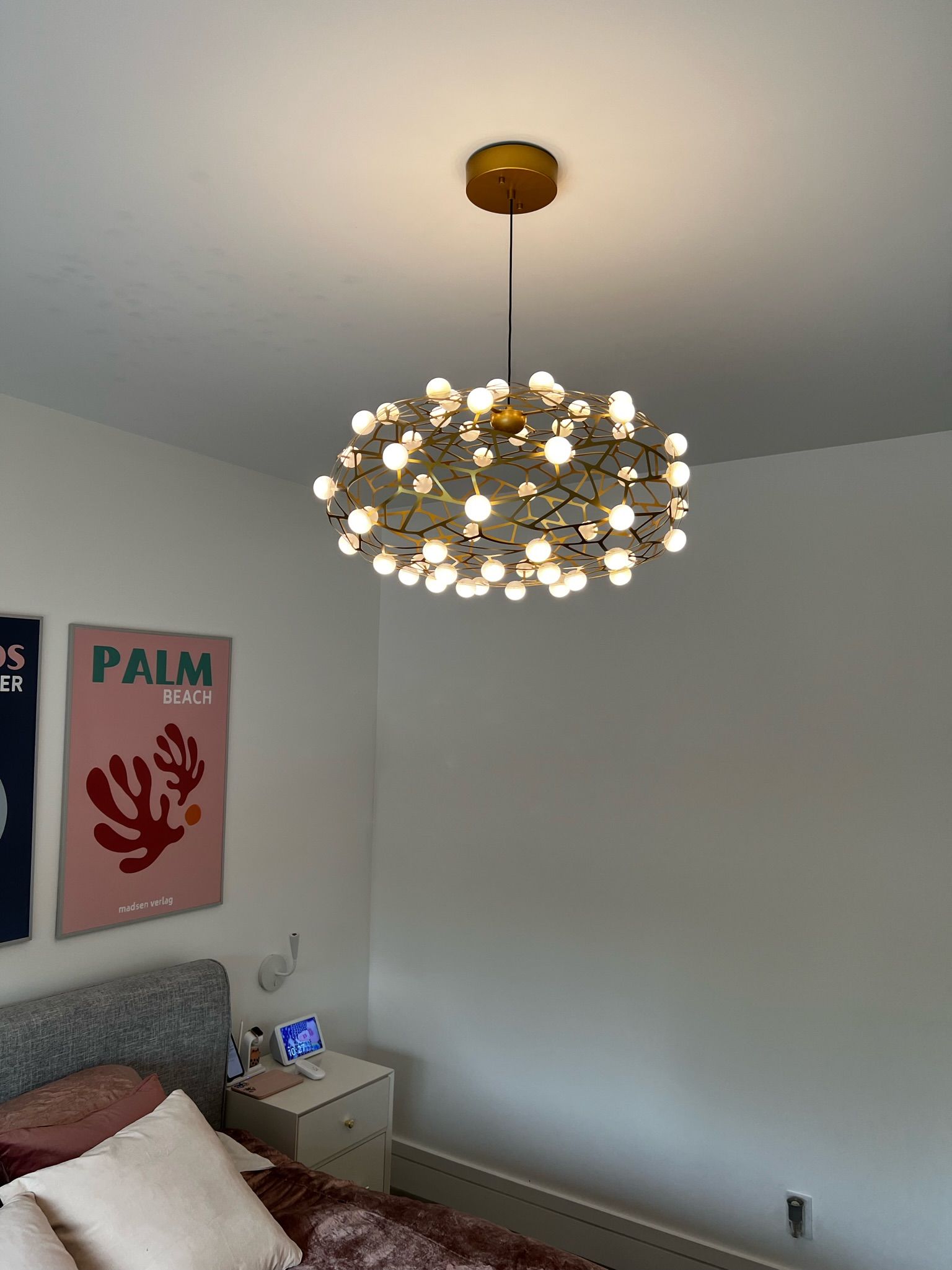 Bedroom with a modern chandelier, two wall art pieces, and a nightstand.