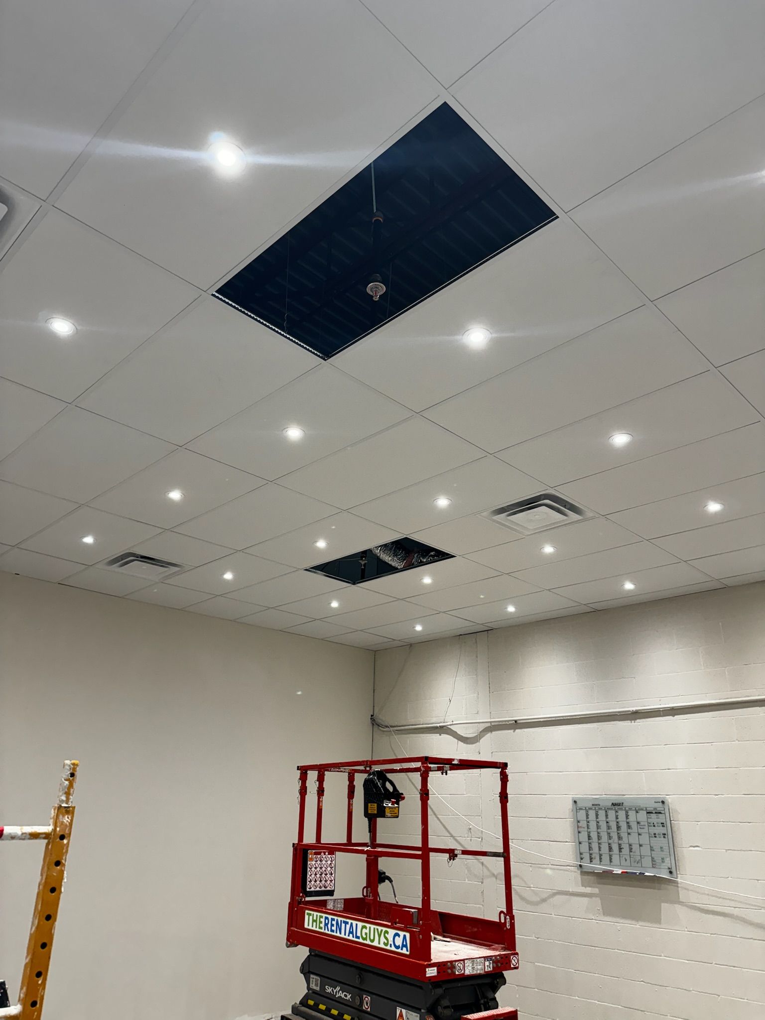 A red lift platform under a ceiling with open panels and lights; electrical work in progress.