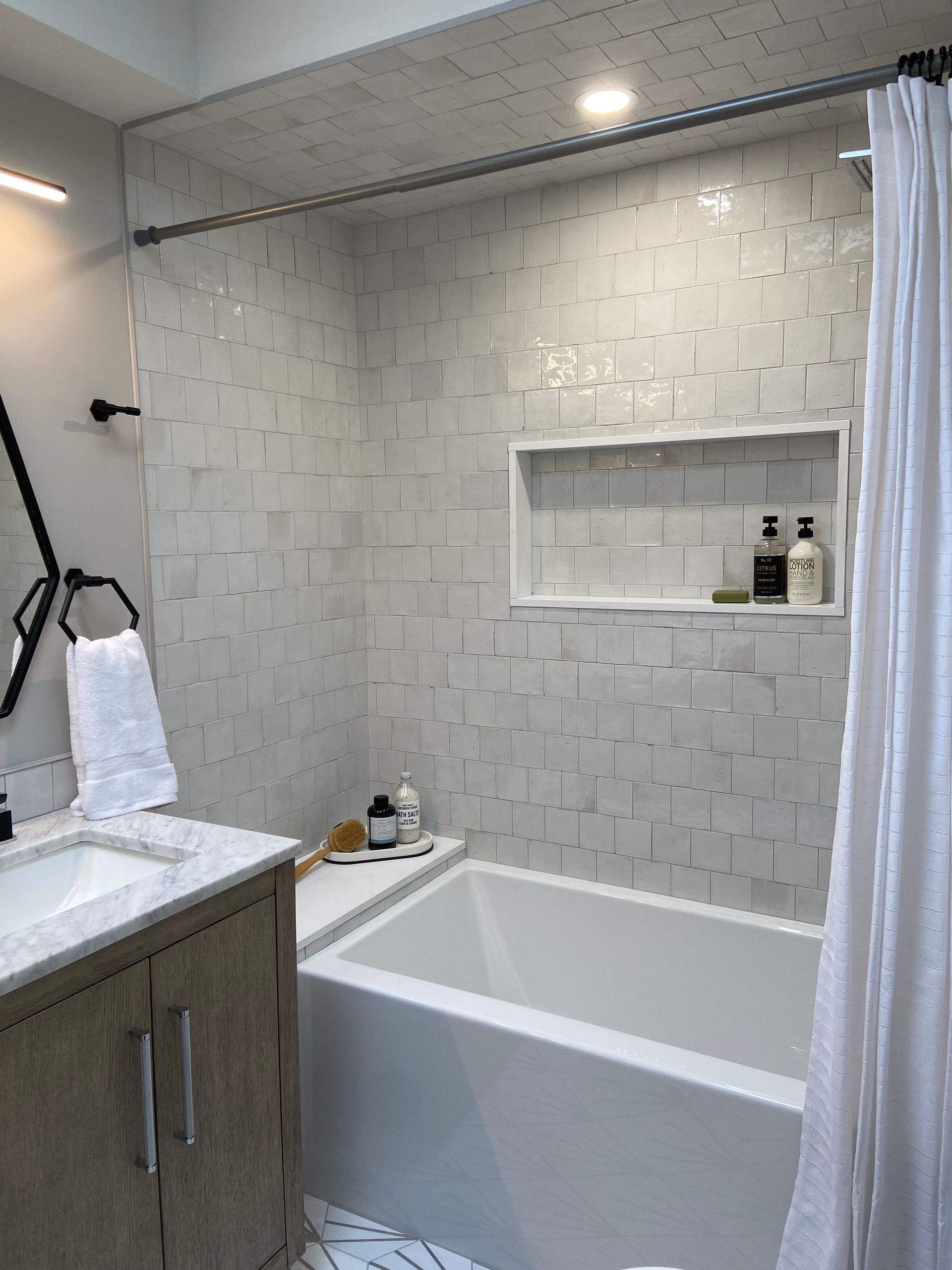 Bathroom with white tile, a bathtub, and a wood-tone vanity.