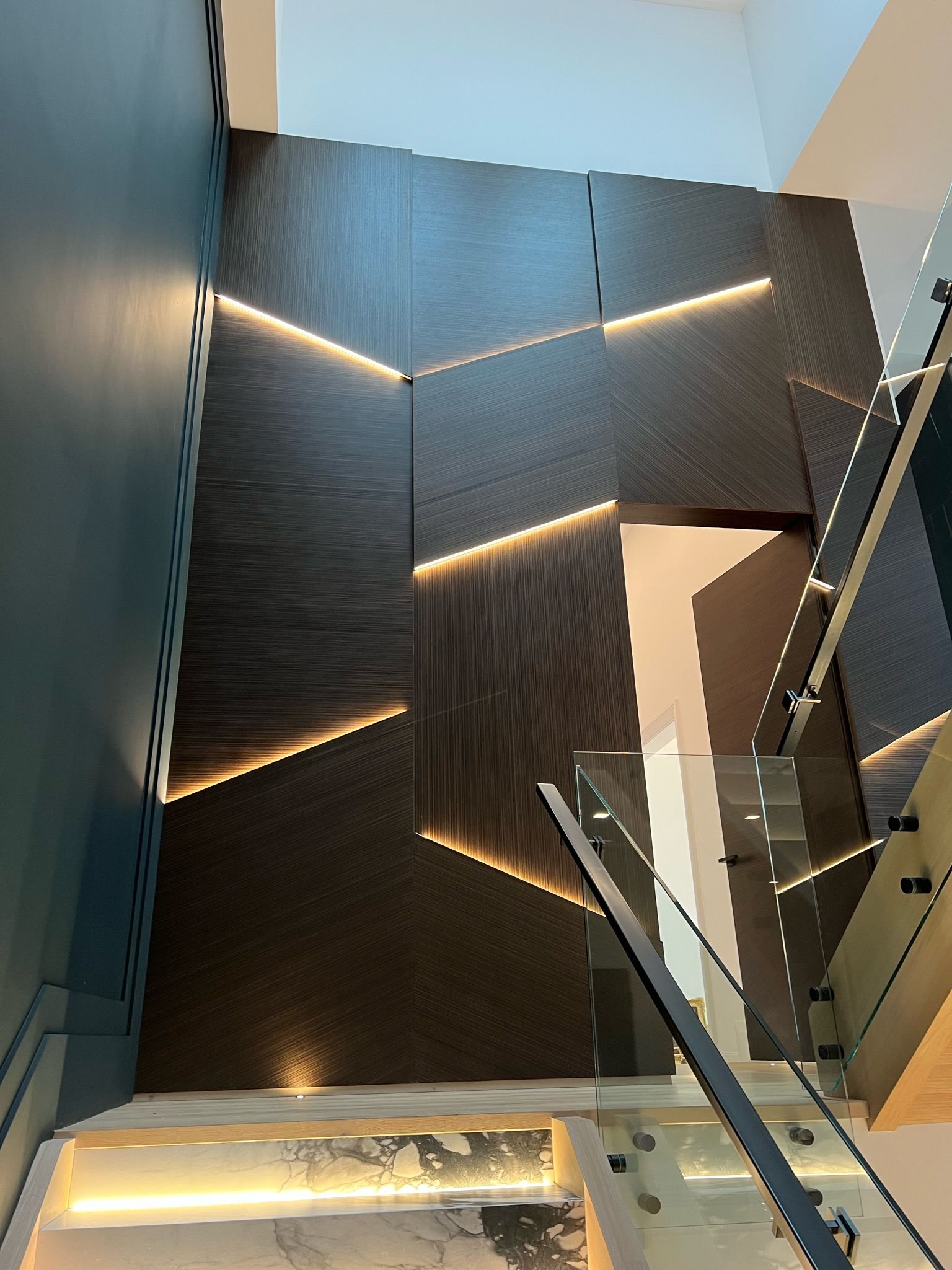 Staircase with dark textured wall, geometric light strips, glass railing, teal wall.
