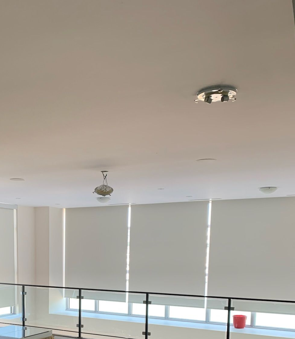 High angle view of a white ceiling with two light fixtures, and windows with closed white shades.