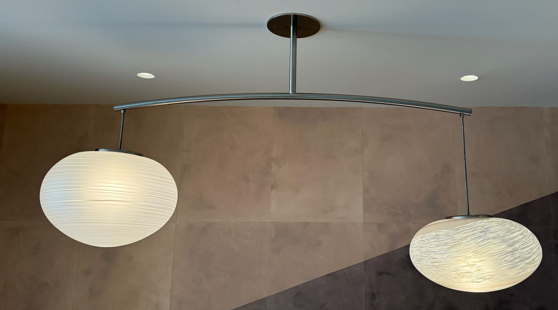 Two globe pendant lights hanging from a curved bar, mounted on a ceiling.