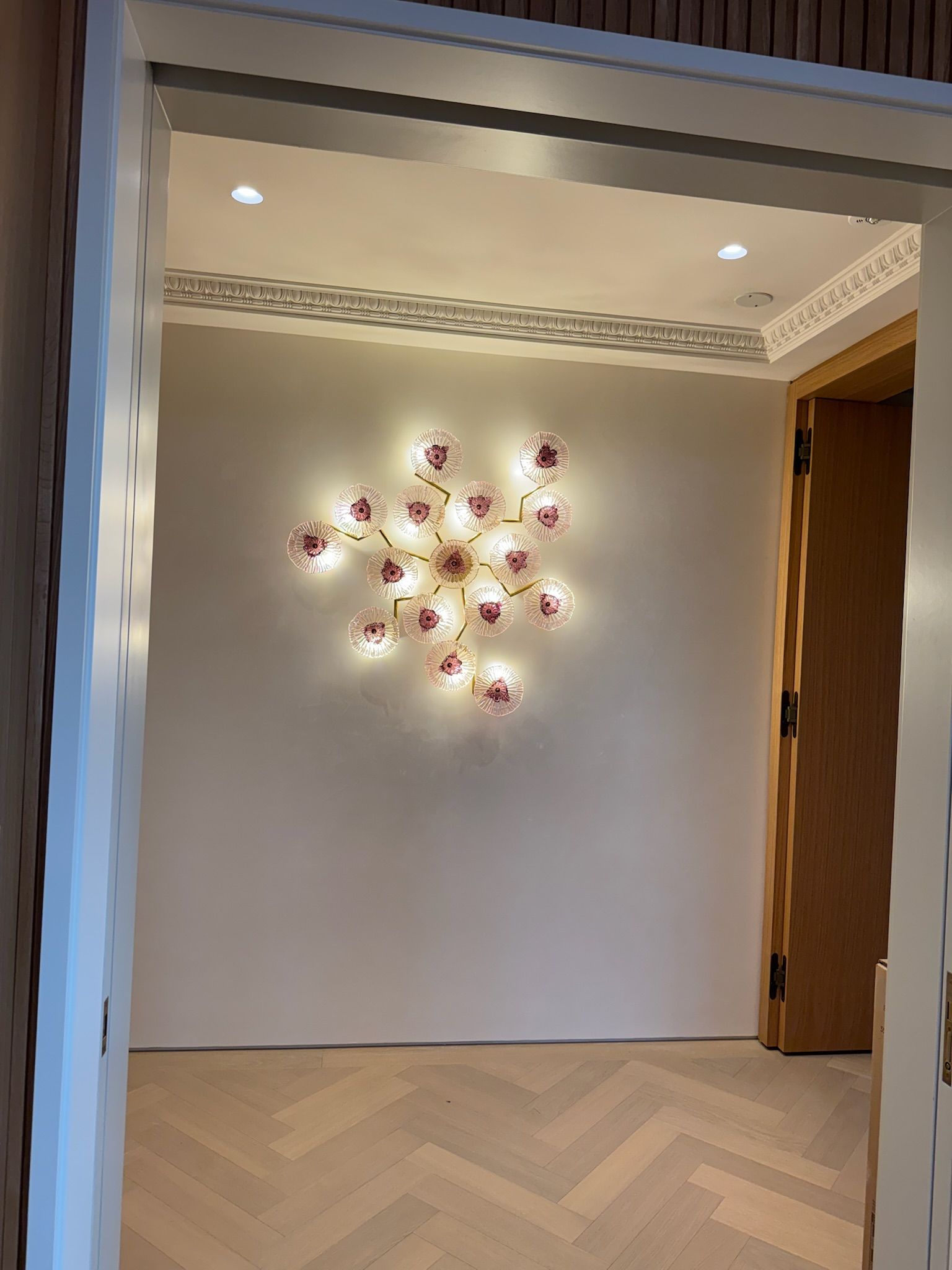Hallway with a flower-shaped wall light on a light-colored wall, with a herringbone wood floor.