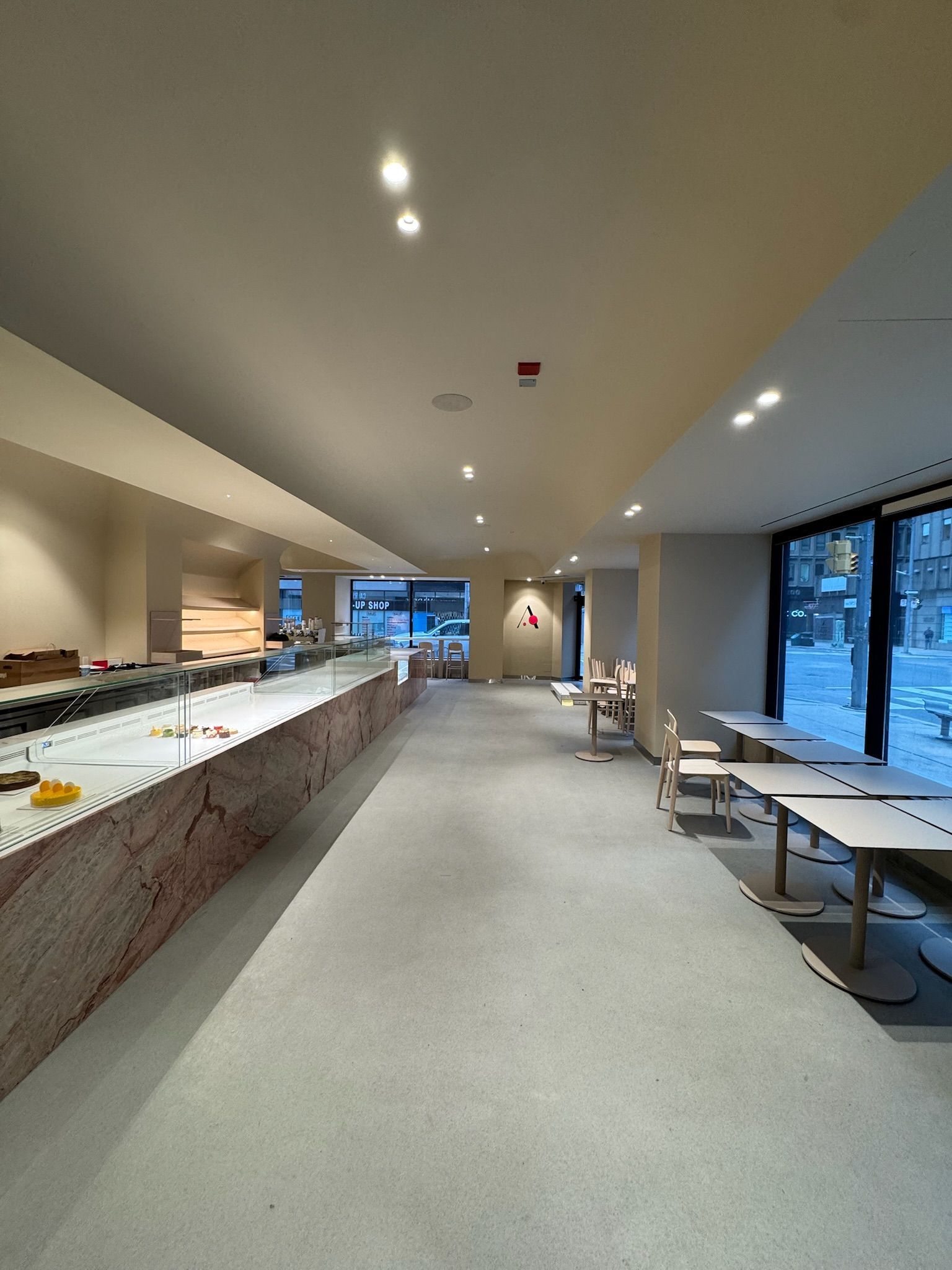 Long, narrow, newly renovated cafe with counter and seating areas; pink stone counter, large windows.